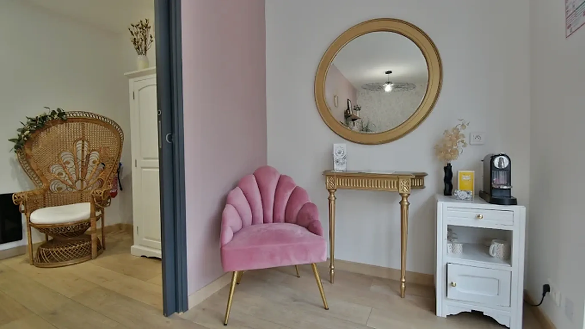 Coin accueil de l’institut avec fauteuil en rotin et miroir rond.